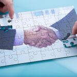 A jigsaw of a handshake being completed by two hands.