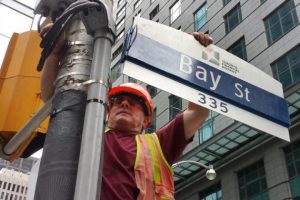 A worker affixes a road sign to the intersection of Bay Street and Adelaide Street in the financial sector of Toronto
