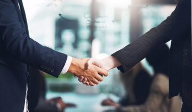 Two men in suits shake hands - only their arms are visible