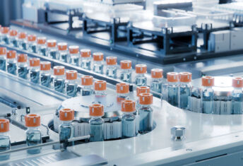 Exclusive: Sheridan acquires Carolina Components Group Vaccine Production Facility. Medication Manufacturing Process. Glass Vials with Orange Caps on Conveyor Belt. Medical Ampoule Production Line at Modern Pharmaceutical Factory.