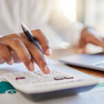 Finance, accounting and fintech, a man on a computer and calculator working out his business budget strategy. Businessman at his office desk, laptop, money management and financial investment online.