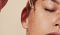 Close-up highly detailed shot of female skin with freckles and pipette with serum. Cropped shot of young woman with smooth perfect skin applying liquid serum on face.