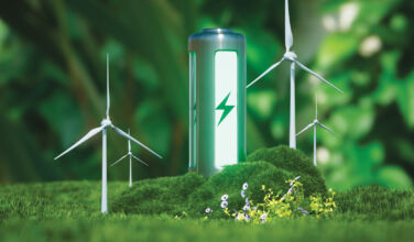 Photo of a green eco-battery surrounded by forestry and windturbines.