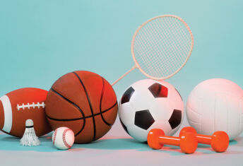 A pile of various sports equipment including a basketball, a shuttlecock and some weights
