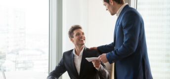 General manager presenting an envelope with premium or bonus cash to male company official. Boss congratulating happy employee with career promotion, thanking for good job and giving financial reward
