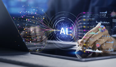 Image of a digital AI button hovering over a laptop, symbolizing the synthesis of data.