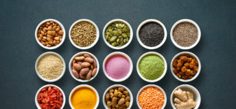 Various colorful superfoods as acai powder, turmeric, matcha green tea, spirulina, quinoa, pumpkin seeds, blueberry, dried goji berries, cape gooseberries, raw cocoa, hemp seeds and other in bowls on dark background